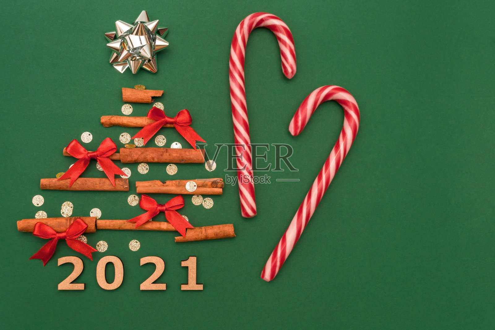 圣诞作文:2021肉桂树,红色蝴蝶结,糖果,圣诞甘蔗糖果在绿色的背景。圣诞节,冬天,新年的概念。平铺,俯视图,拷贝空间照片摄影图片