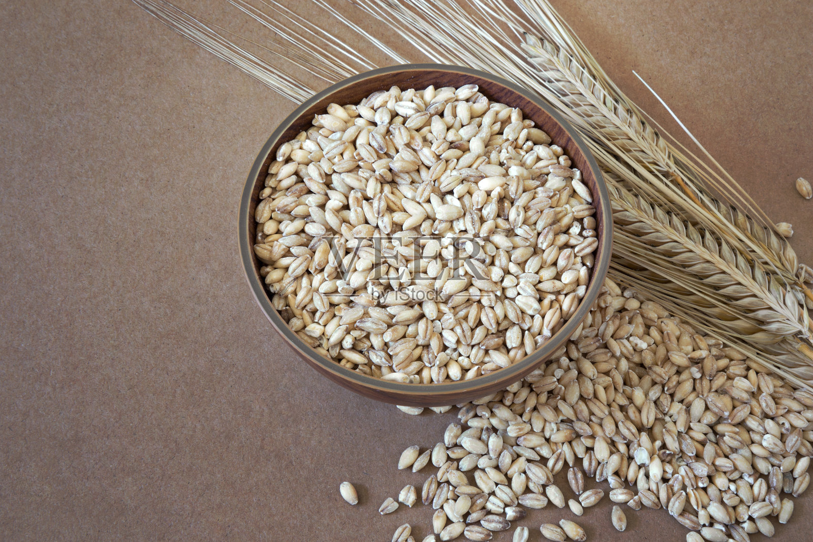 生的去皮大麦粒(粗大麦)放在一个木碗里,背景是棕色。照片摄影图片