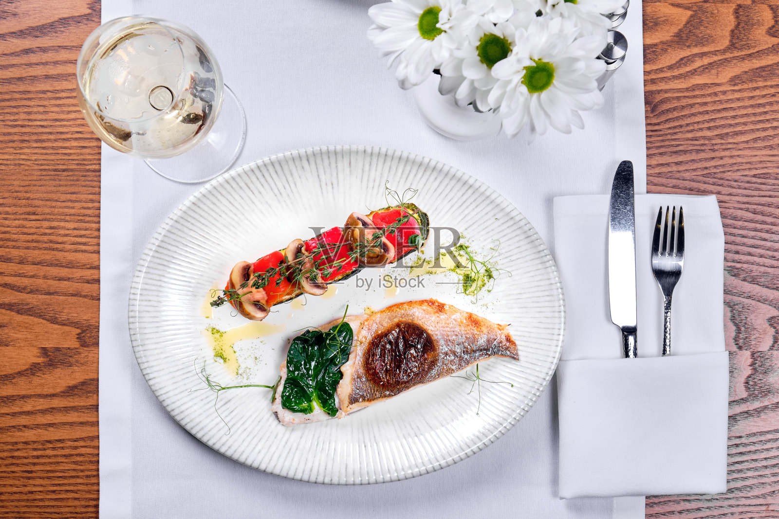 桌上放着一盘鲈鱼和一杯葡萄酒。从以上观点。照片摄影图片