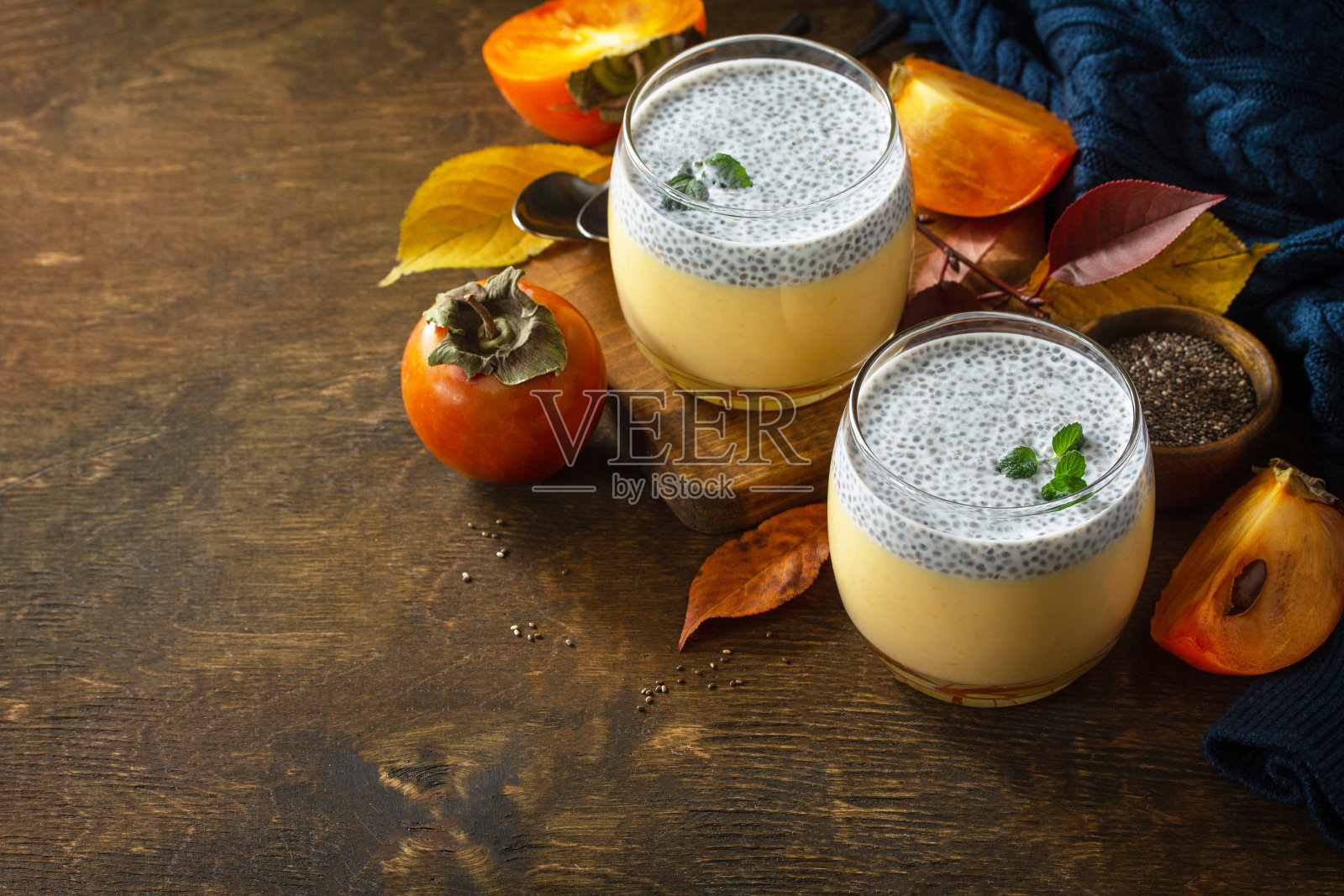 秋天的甜点。木桌上放着自制的意式奶冻,配上柿子和奇异子。副本的空间。照片摄影图片