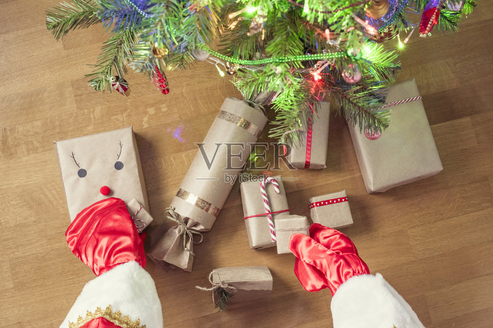 圣诞老人把手工制作的礼物包在牛皮纸下放在圣诞树下。提出了家庭。前视图。平的。照片摄影图片