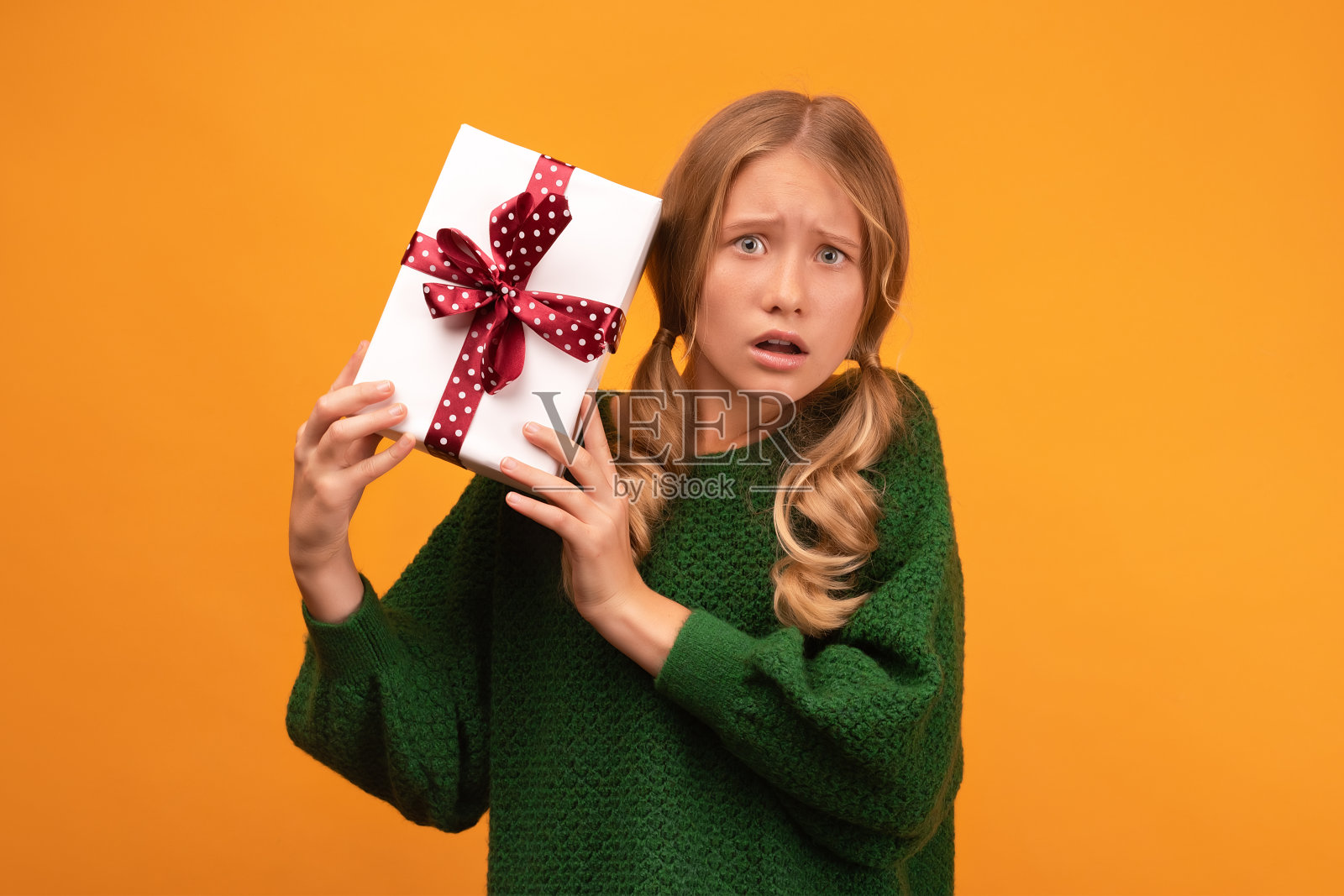 迷人的金发女孩12-14岁拿着红蝴蝶结礼物盒的形象。工作室拍摄,黄色背景,孤立照片摄影图片