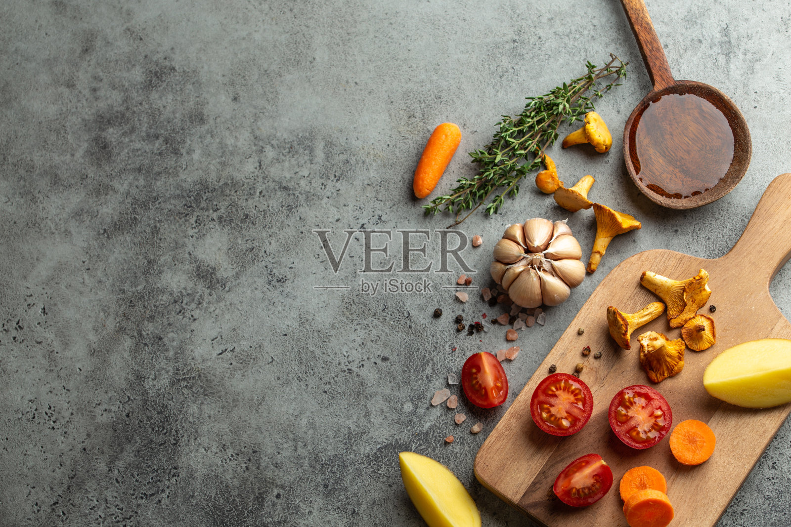 新鲜的圣女果、土豆、蘑菇、鸡油菌、胡萝卜、香草放在切菜板上,用木勺蘸橄榄油。食材烹饪背景,俯视图,文字空间照片摄影图片