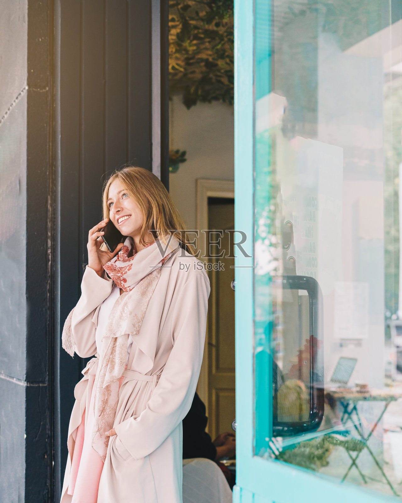 一个漂亮的金发女孩在咖啡店门口打电话。照片摄影图片
