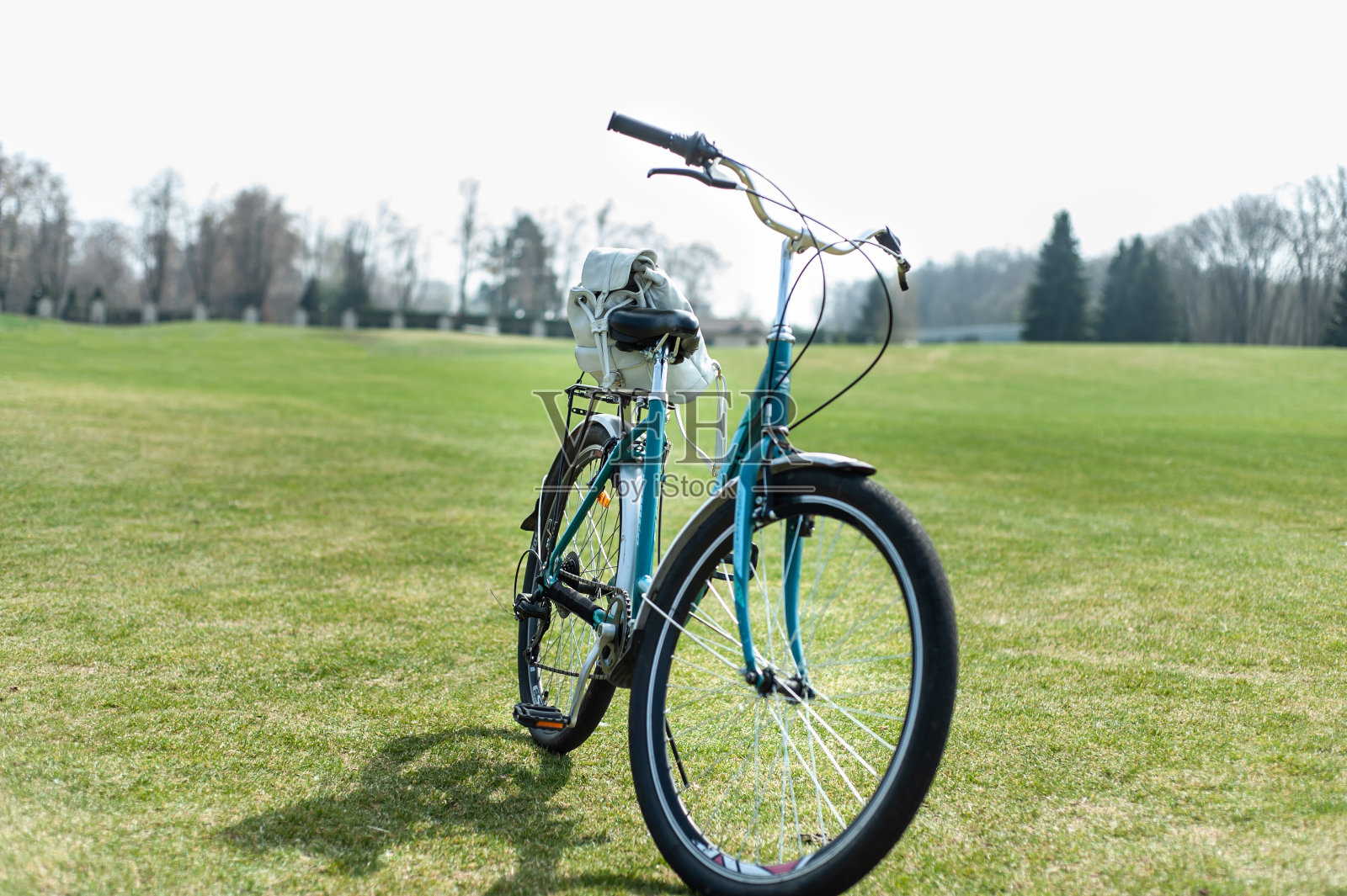 初春时节,绿色妇女的自行车,行李箱上背着白色的小背包,停在绿色的草坪上照片摄影图片