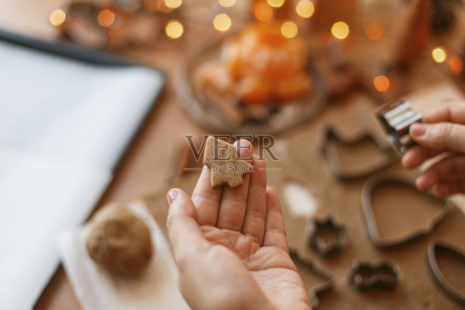 一个人拿着树姜饼曲奇饼,背景是节日的灯在乡村的桌子上。圣诞节照片摄影图片