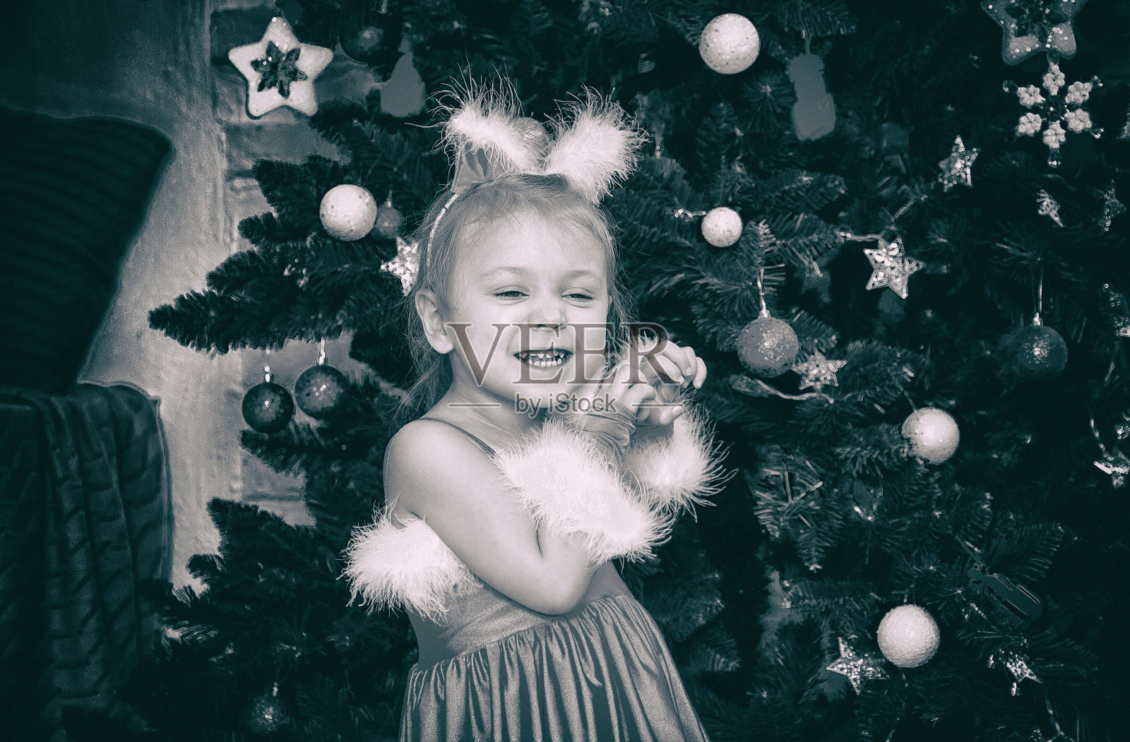 圣诞,新年树。一个穿着毛茸茸的红色衣服,头上戴着耳朵的小女孩正站在圣诞树下。照片摄影图片