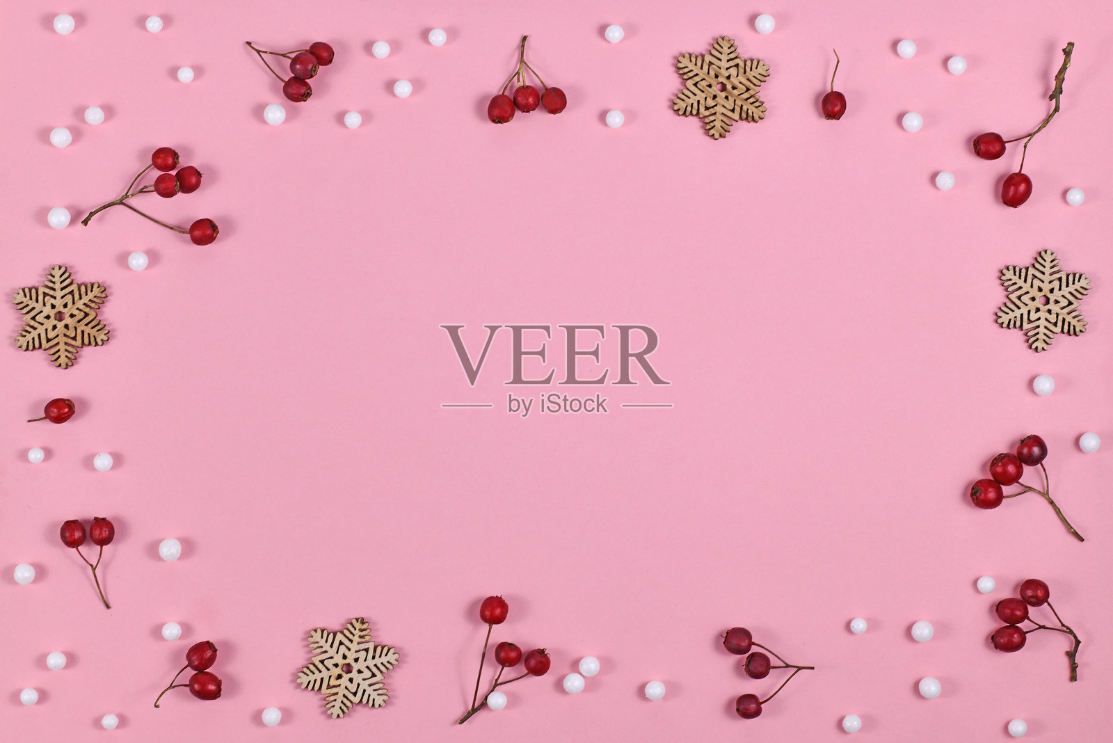 季节性的红色冬季浆果和木制雪花装饰形成框架周围的浅粉色背景照片摄影图片