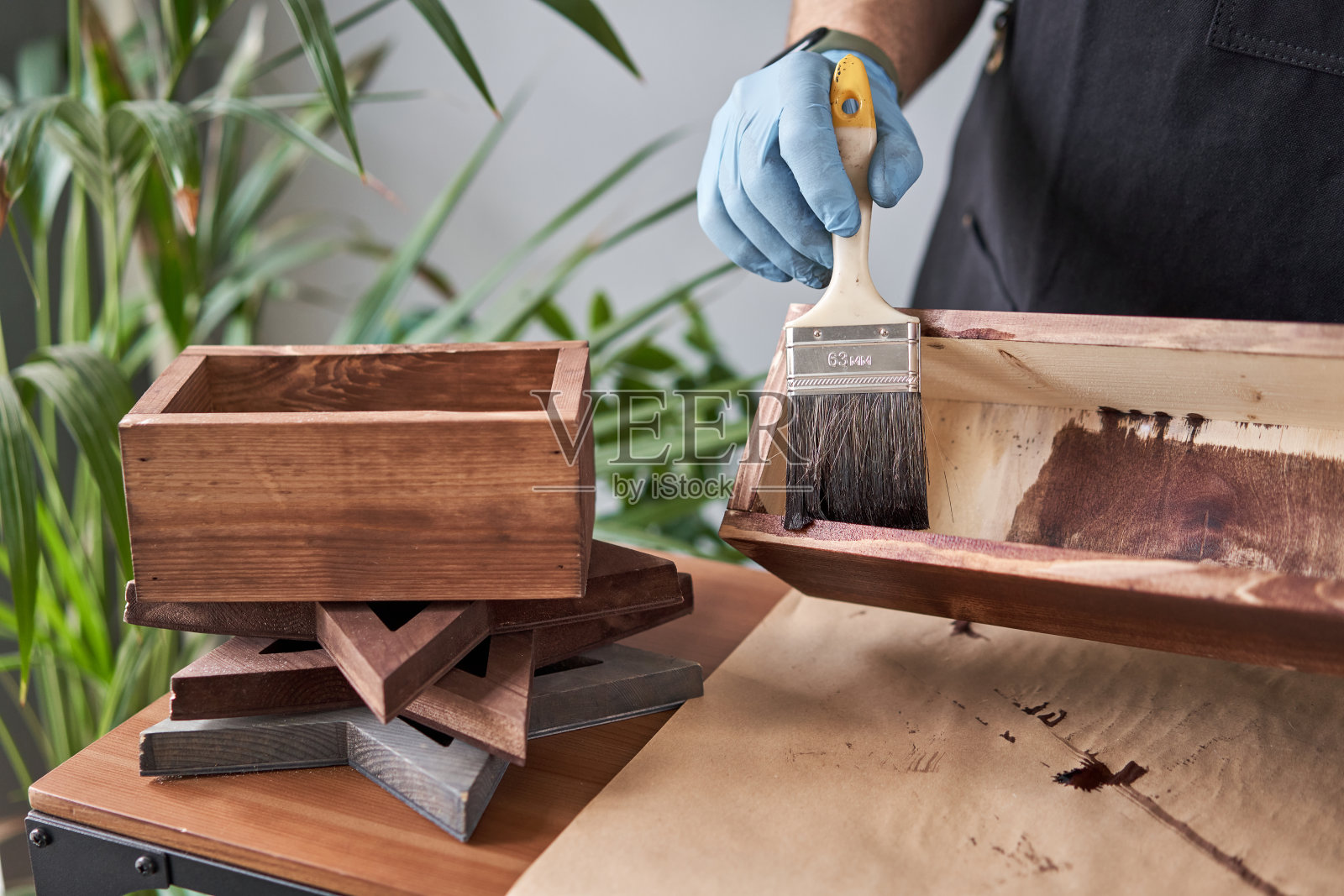 在她的小商木工车间里,一名木匠用刷子给花板条箱上漆。在您的作品中,您是否使用污渍或木材防腐剂来显示木材的图案。照片摄影图片