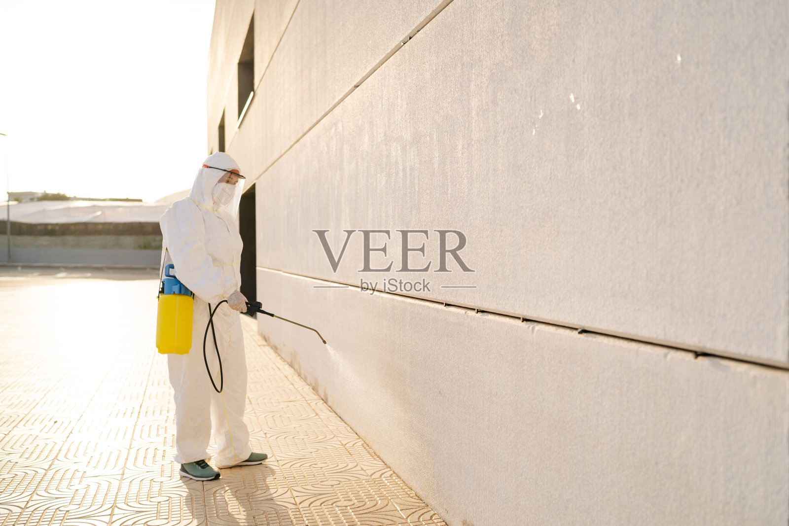 穿着病毒防护服和口罩的人正在用喷雾器对建筑物进行消毒照片摄影图片