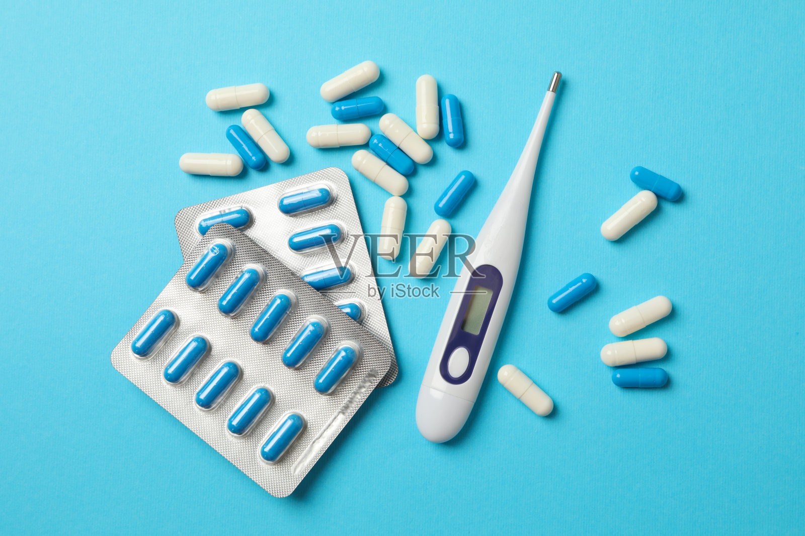蓝色背景上的电子温度计和药片照片摄影图片