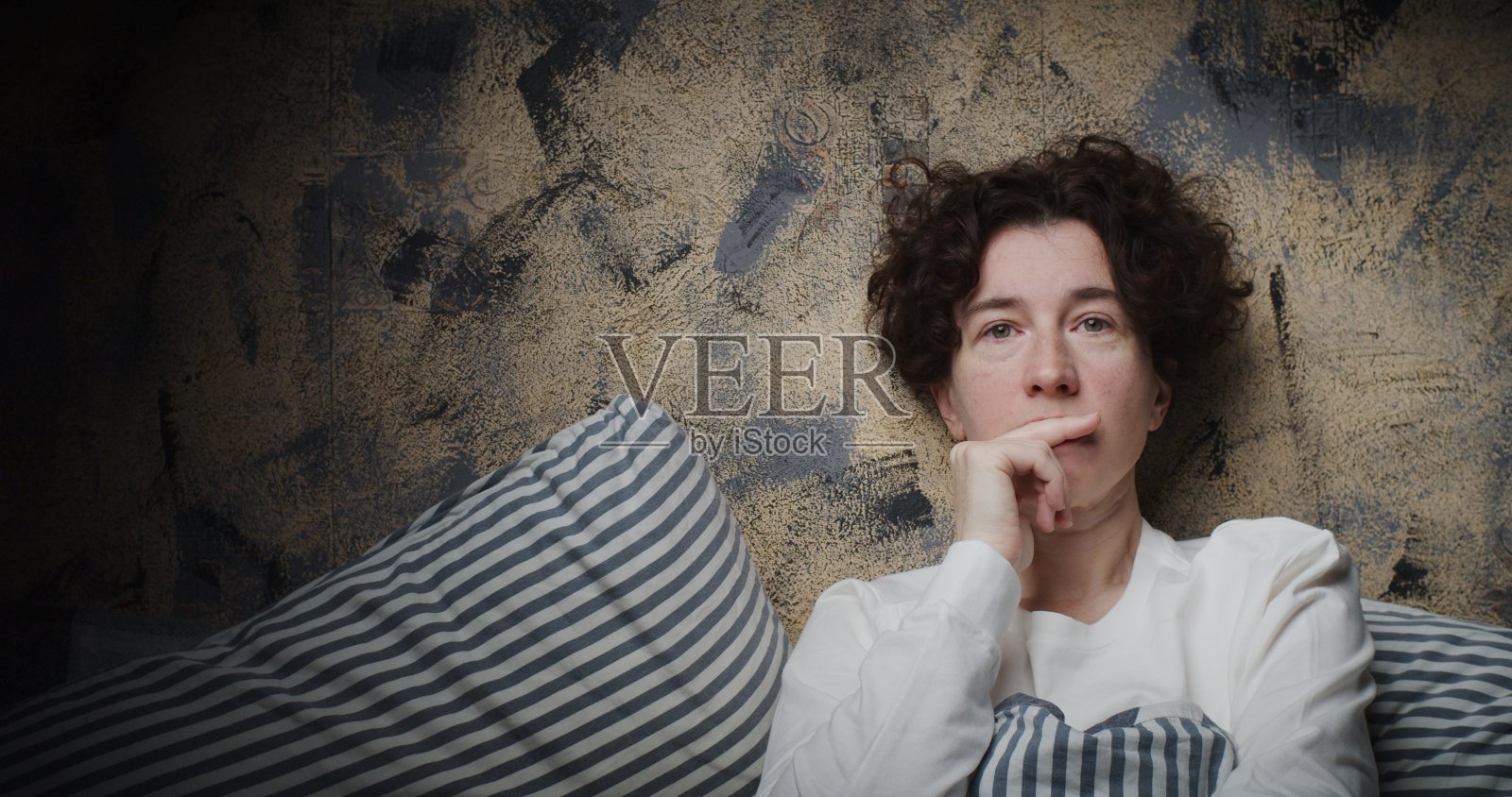 一个成熟女人坐在床上沉思时揉她的嘴唇的腰部肖像照片摄影图片