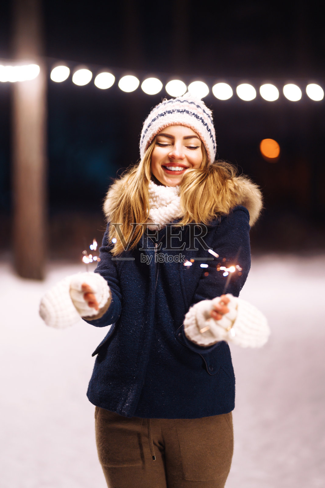 在冬天的森林里,一个快乐的年轻女子手里拿着一个烟火。照片摄影图片