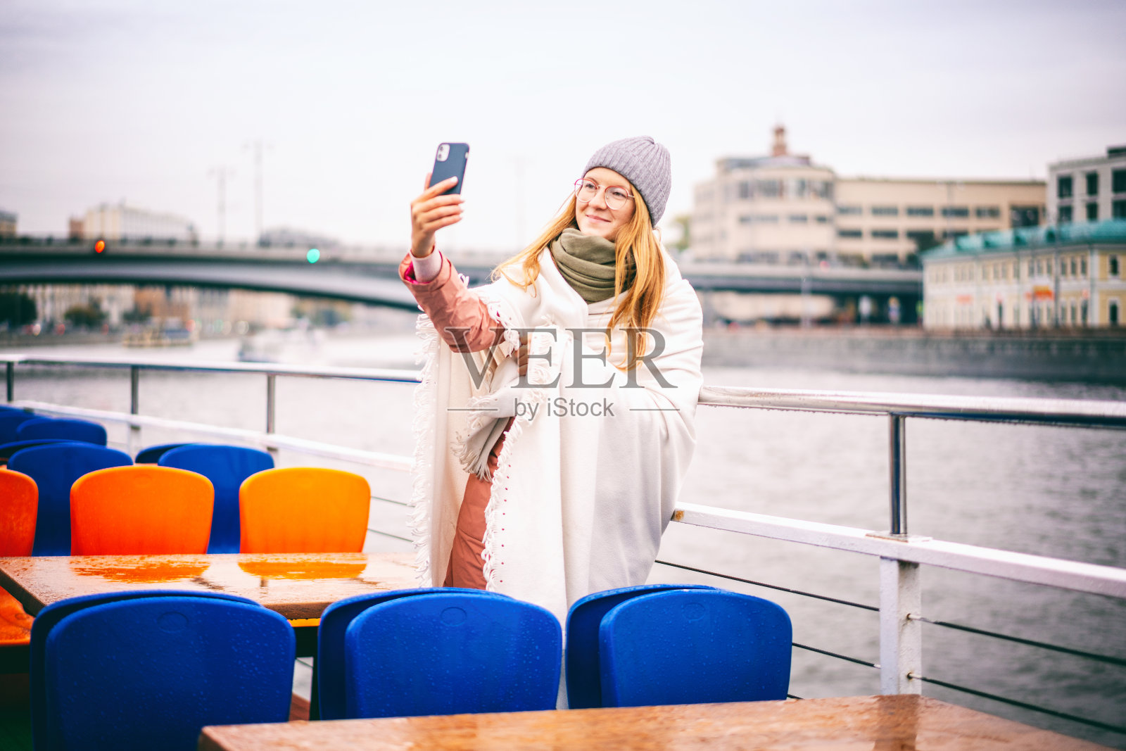 一名戴着眼镜、头戴帽子、身穿夹克的红发女子在莫斯科市中心河上的游船上自拍照片摄影图片