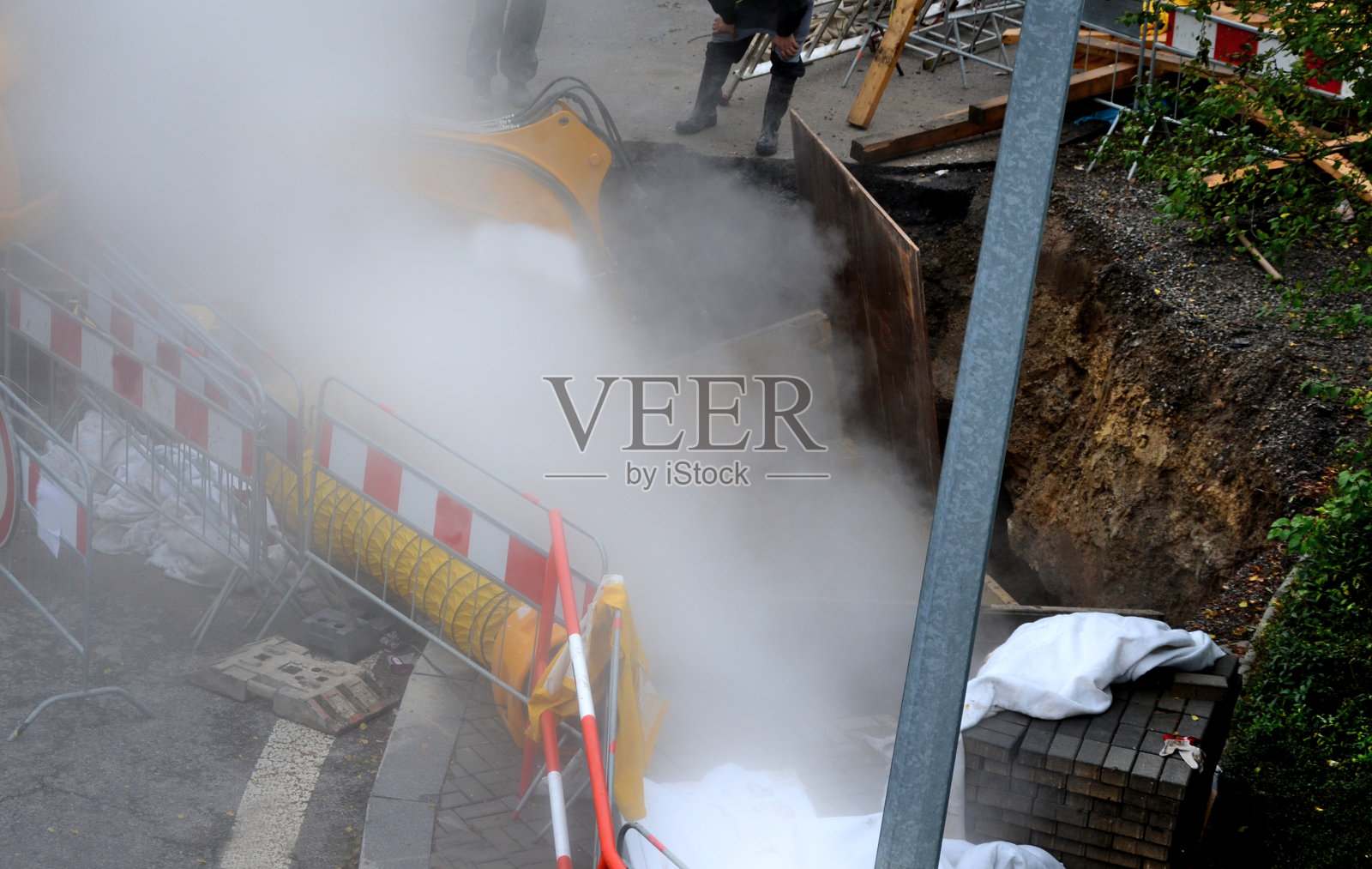 用热水或蒸汽在一个深的装甲坑中修理管道,这个坑类似于一个滚动着雾或灰尘的矿井。用临时建筑围栏围起来以防止进入照片摄影图片