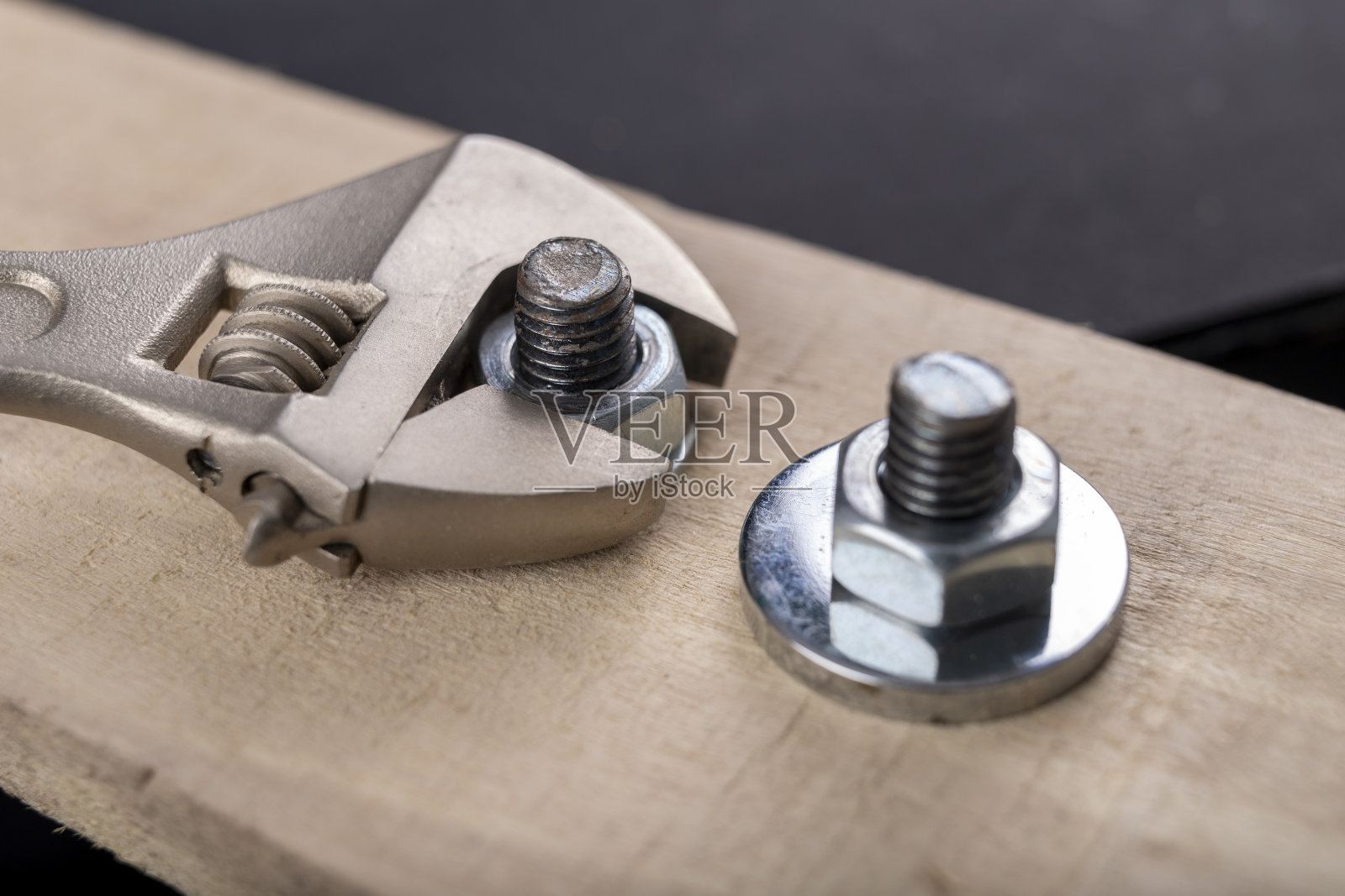 用于连接木材的金属螺栓和螺母。用活动扳手拧紧螺丝。黑暗的背景。照片摄影图片