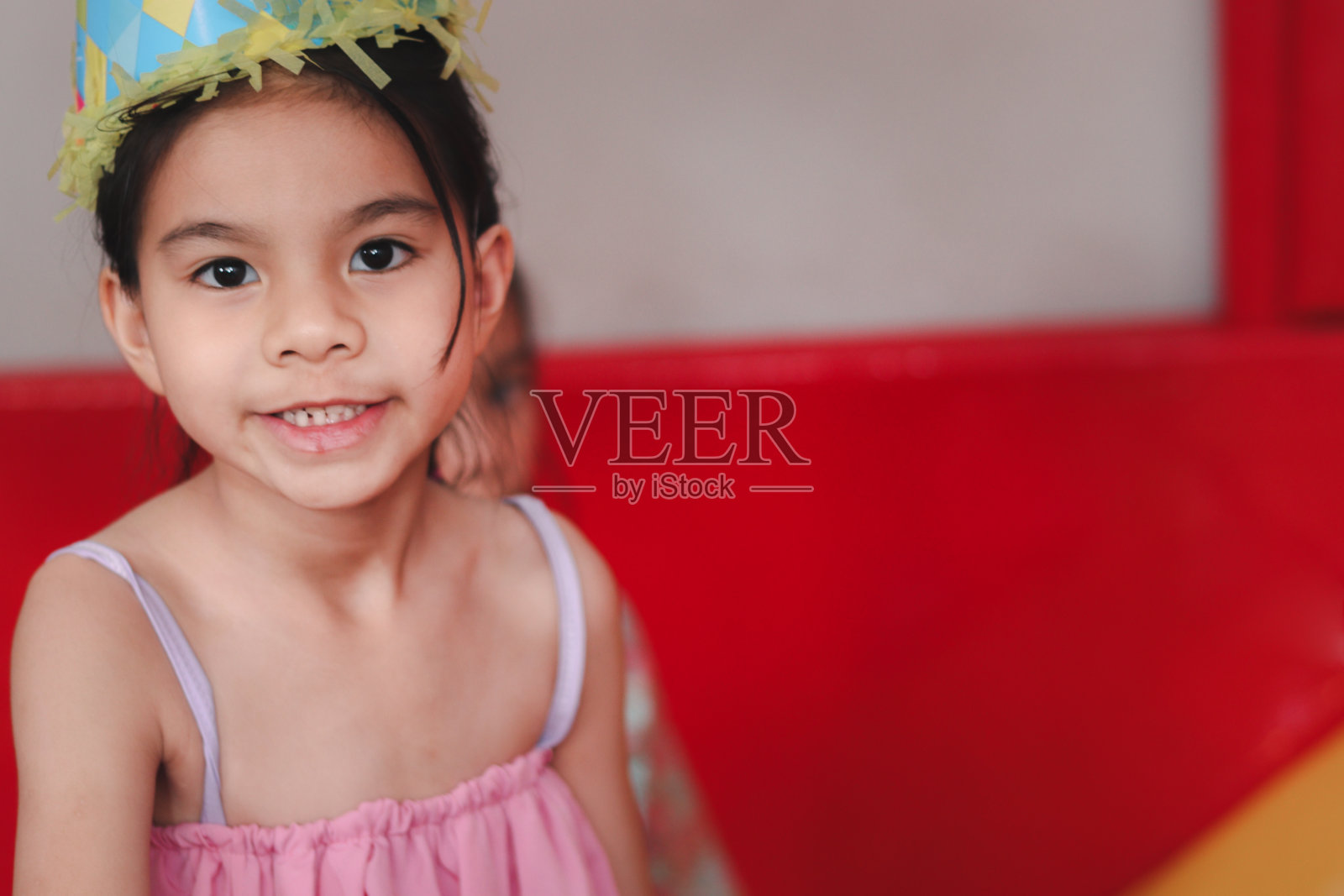 美丽的女孩的肖像与黑色的长发戴生日帽,在操场上玩,孩子有乐趣和玩的朋友。照片摄影图片