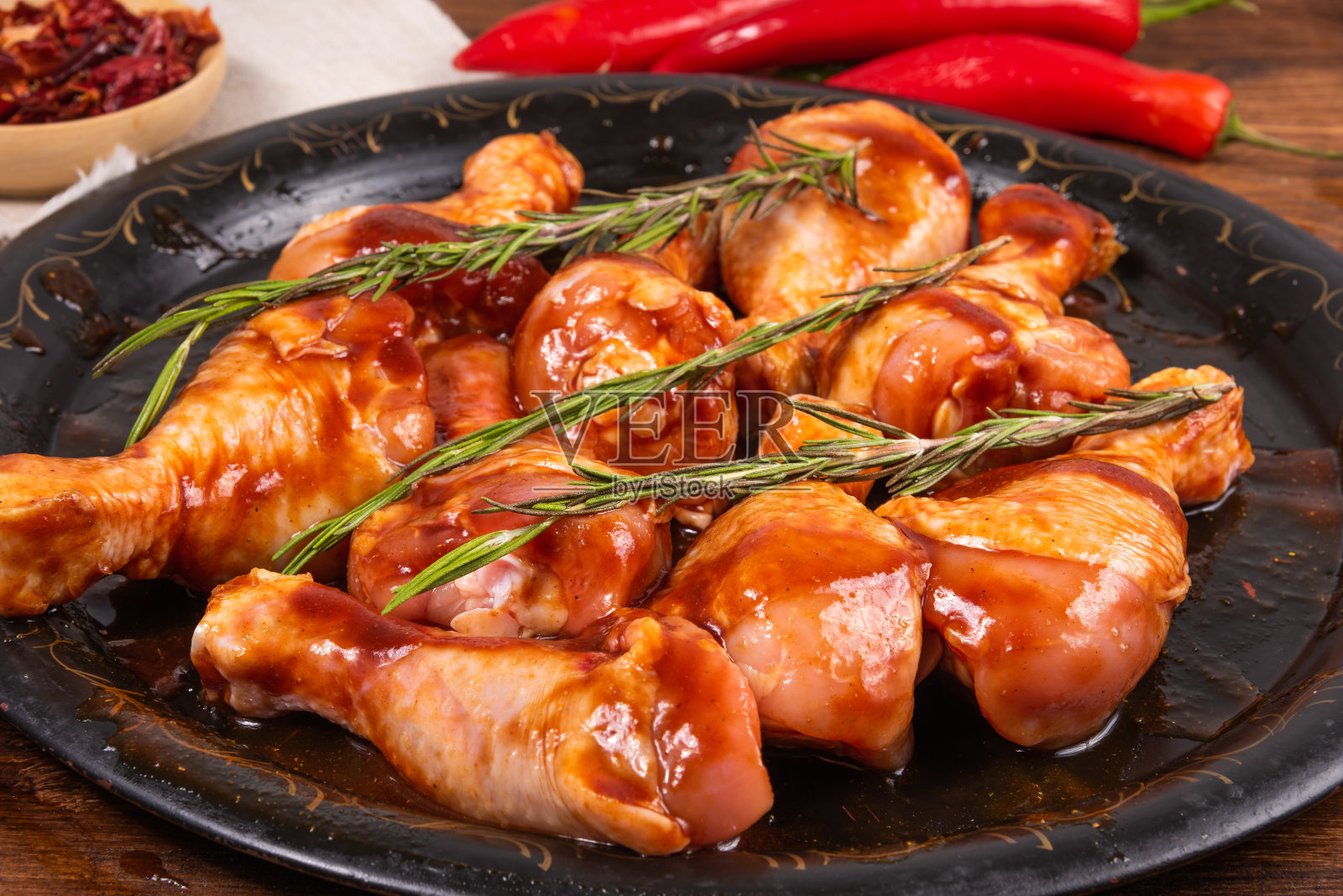 生鸡腿浸泡在辣汁和香料的黑色煎盘上,特写照片摄影图片