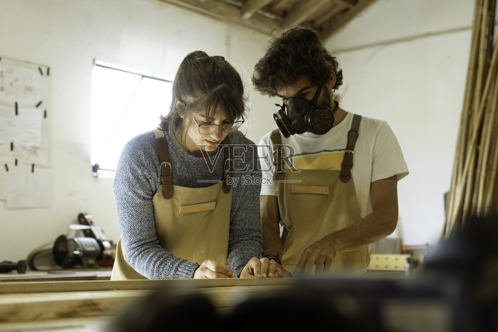 一对年轻的木匠夫妇在一个车间里用木头制作家具,用于室内设计。照片摄影图片