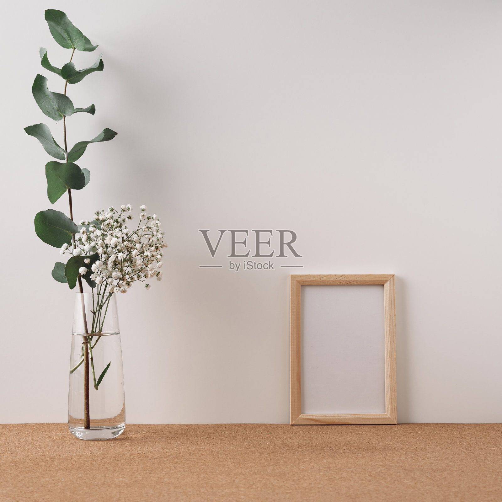 软木塞上放着一个画框和一个花瓶,上面有桉树和白花,背景是白色的。模拟,复制空间。民间。照片摄影图片