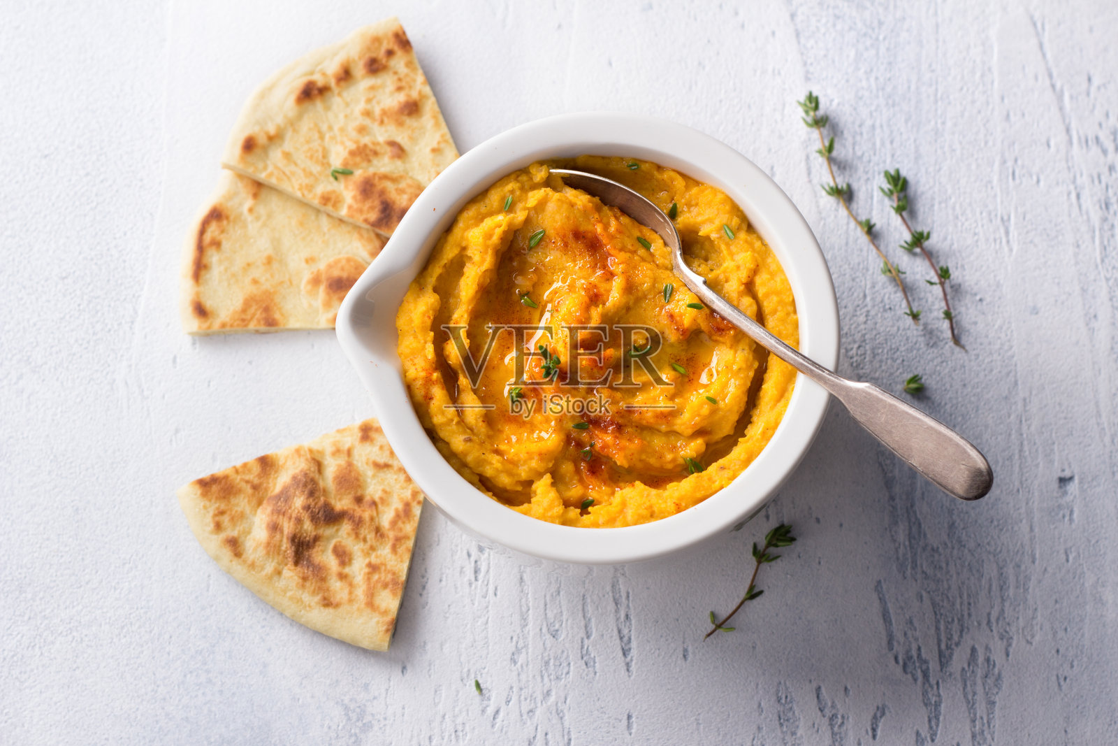 美味健康的自制豆鹰嘴豆泥配烤南瓜,芝麻酱和香料,浅蓝色背景上的扁面包照片摄影图片