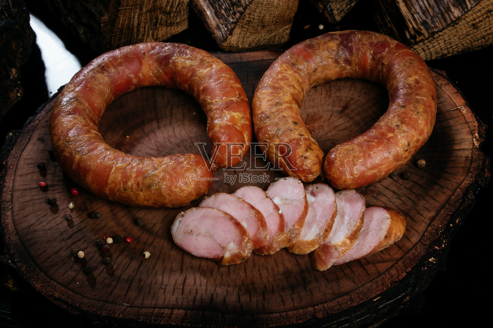 两圈熏香肠放在一块木板上,背景是烧过的柴火。几片香肠切片。照片摄影图片