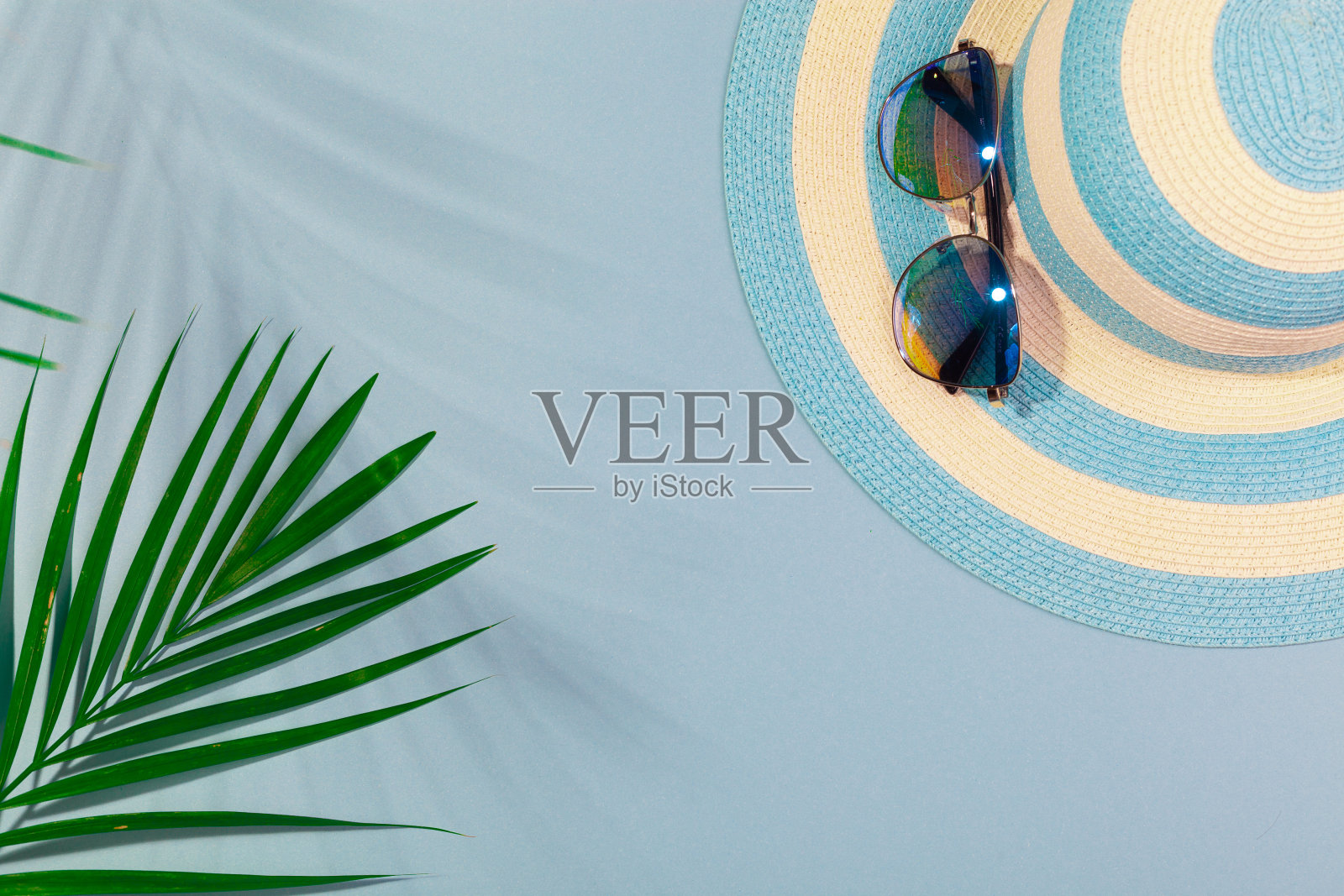 在绿松石蓝色背景的海滩配件俯视图-太阳镜,蓝色条纹帽子和棕榈叶。概念海滩度假,海上旅游,温暖阳光灿烂的夏天。广告空间照片摄影图片