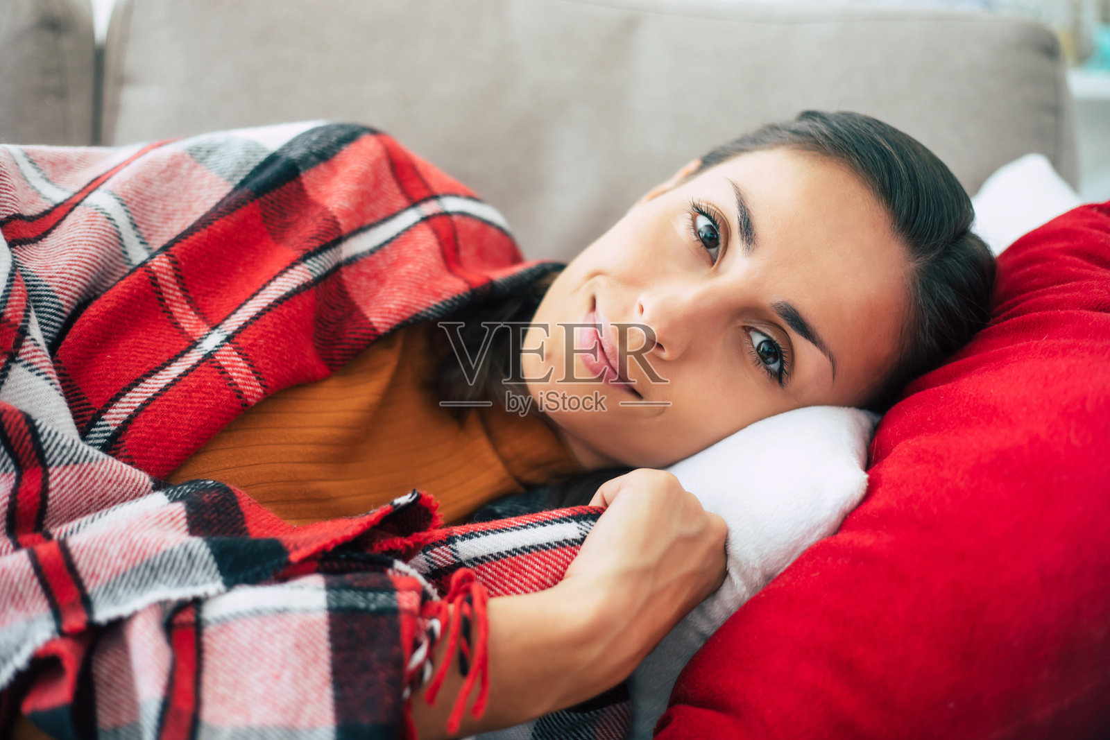 美丽可爱的年轻女子正躺在格子格子的沙发上,在冬日里放松。照片摄影图片