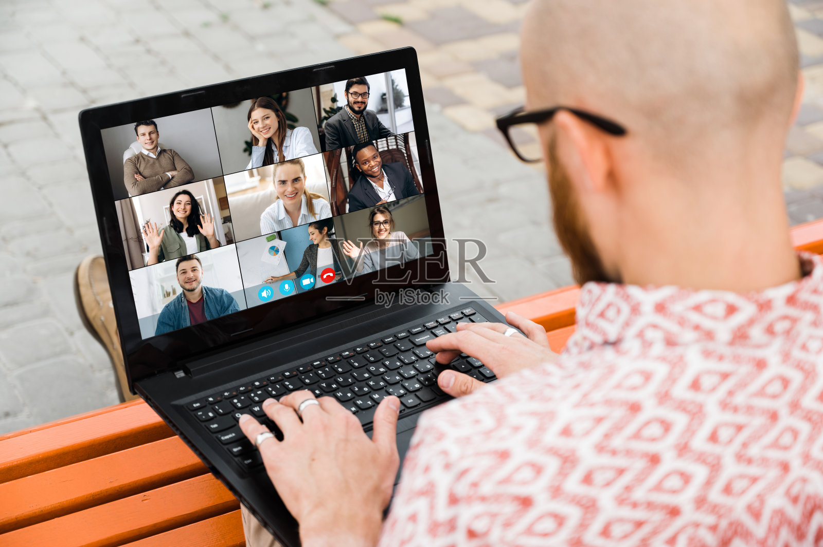 在线学习。一个拿着笔记本电脑的学生的后视图。他通过视频会议在网上学习用笔记本电脑。在笔记本电脑的屏幕上,老师正在教他的学生照片摄影图片