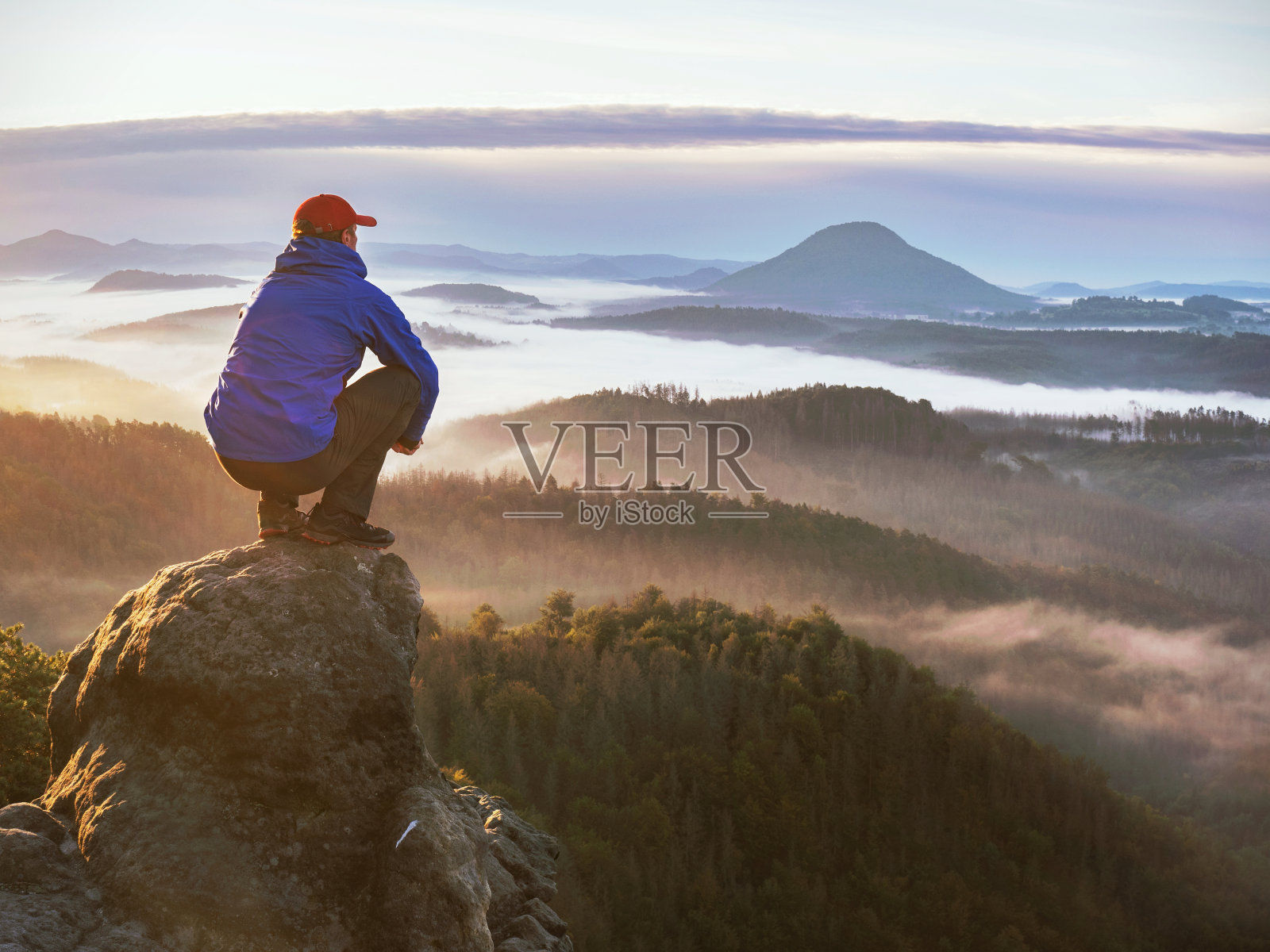 徒步旅行者坐在岩石上,看着五彩缤纷的薄雾照片摄影图片