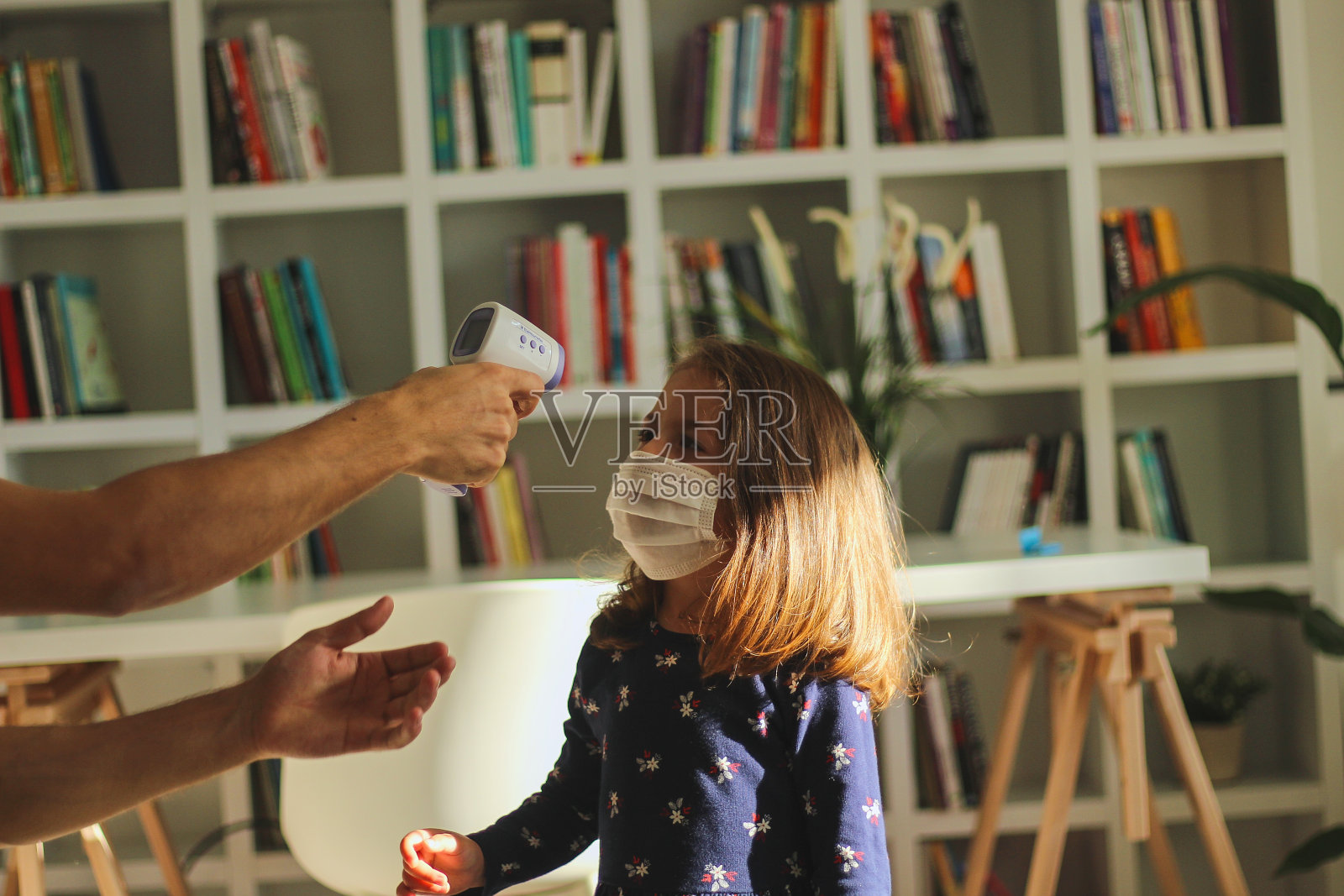 一个年轻人在测量一个戴着防护面具的女孩的体温照片摄影图片