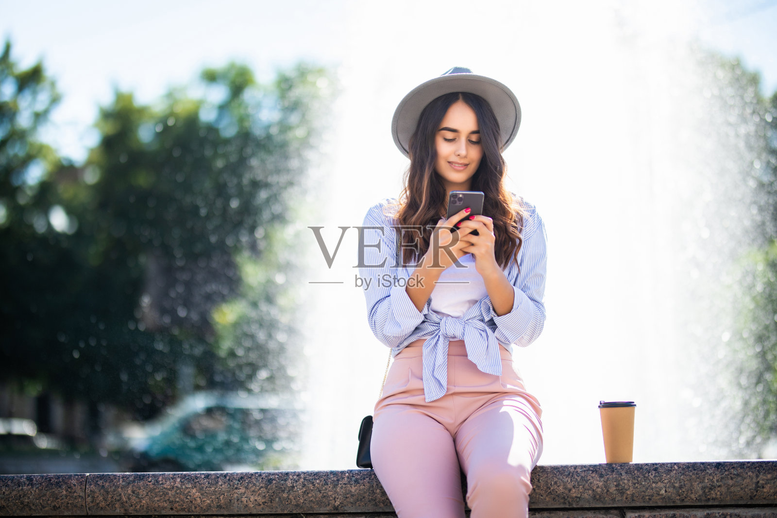 年轻女孩在喷泉附近的街边咖啡杯上用手机上网照片摄影图片