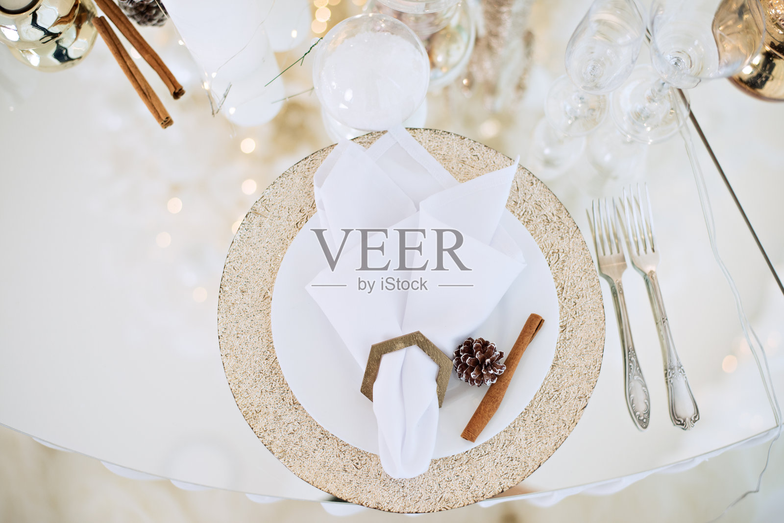 新年喜庆玻璃餐桌摆设。贺卡。在圣诞树的树枝上有香槟杯,餐具,镀金的盘子,餐巾环。用金蜡烛装饰。本空间照片摄影图片