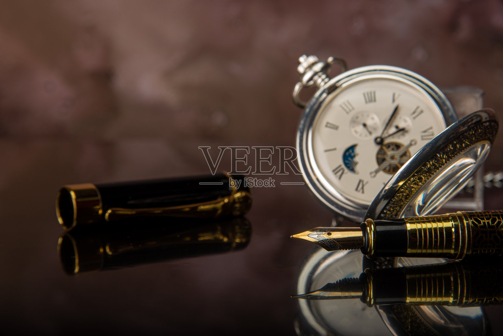 钢笔和怀表在镜面上,背景模糊,选择性聚焦。照片摄影图片