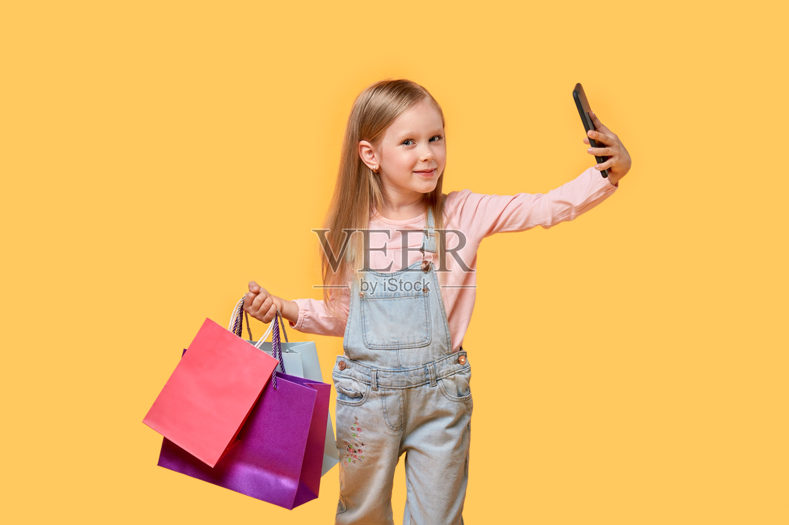 一个女孩手里拿着手机,在五颜六色的袋子里购物。照片摄影图片