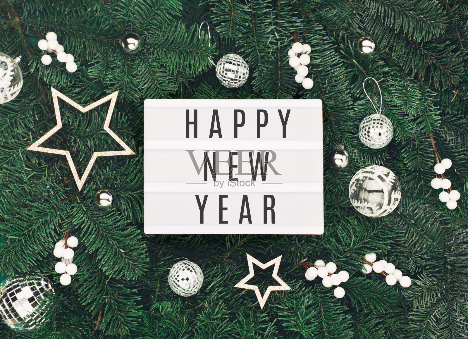 新年快乐的文字在白色灯箱与节日的银白色装饰,橡果在圣诞树的树枝上的背景。照片摄影图片