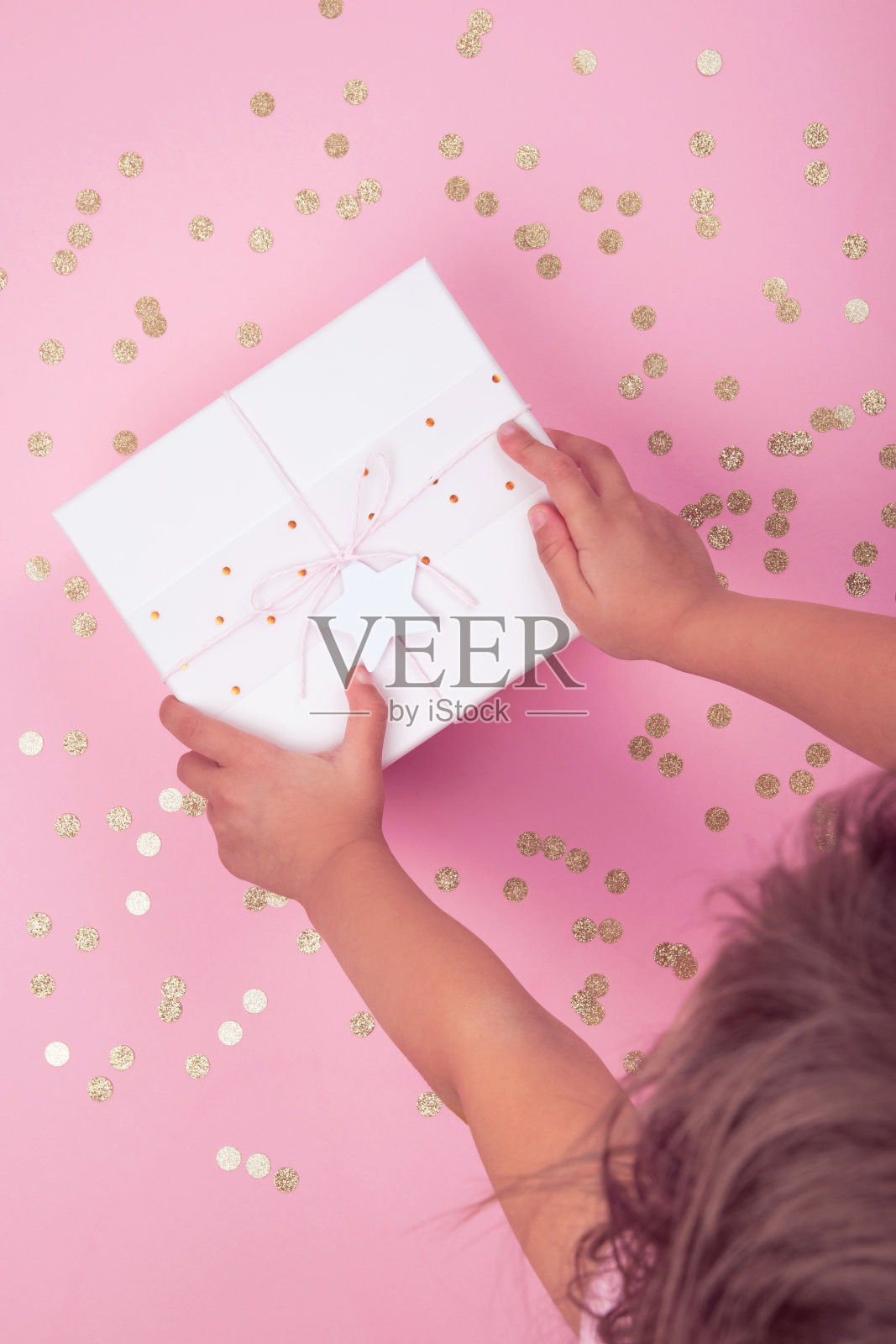 俯视图的孩子手持粉红色礼盒与蝴蝶结和星星的背景装饰与金色的五彩纸屑。照片摄影图片