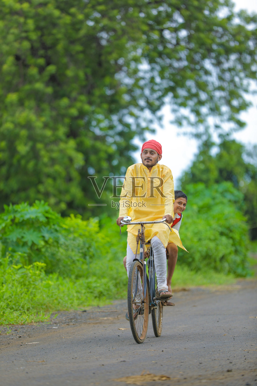 年轻的印度农民和他的儿子骑自行车上学照片摄影图片