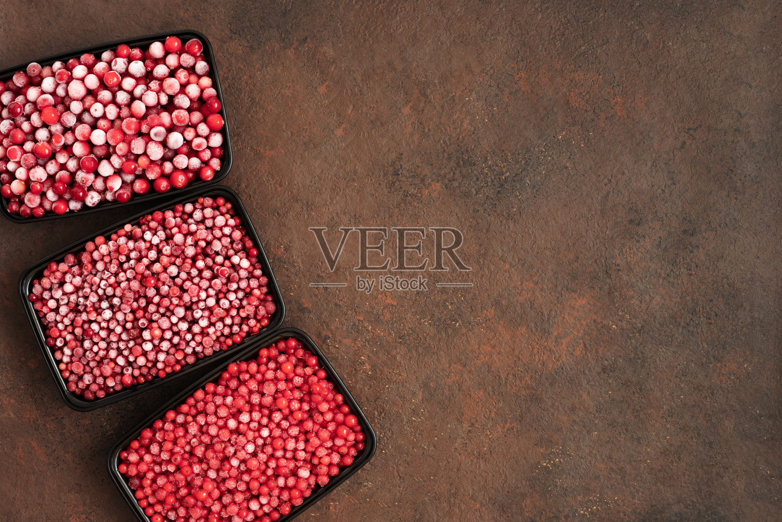 在棕色背景的容器中冷冻浆果。混合浆果,蔓越莓,红加仑子,越橘。冷冻食品。拷贝空间,俯视图。照片摄影图片