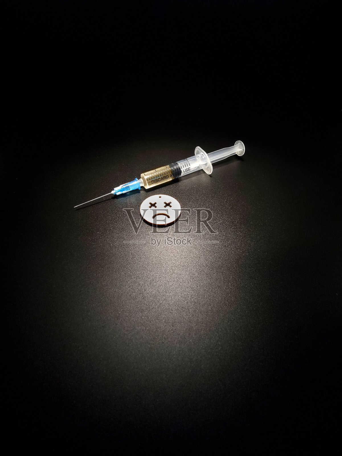带着针的医疗注射器,黑色背景上带着悲伤的微笑照片摄影图片
