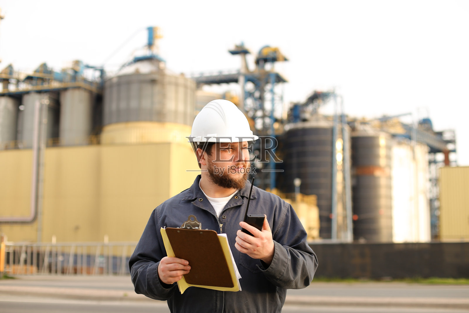 白人工程师拿着对讲机和笔记,背景是工厂照片摄影图片