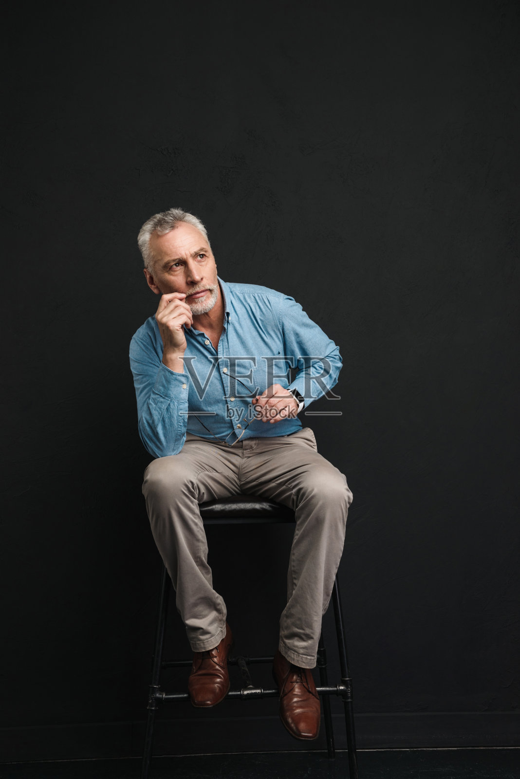 全长照片的白种男性退休60岁与灰色头发和胡子坐在椅子上看一边沉思的观点,孤立在黑色的背景照片摄影图片
