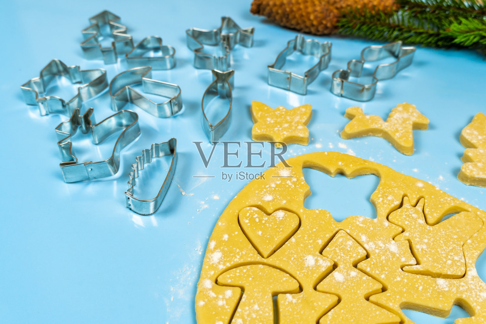 饼干切割器在薄薄滚动的面团上,靠近云杉树枝和橘子在蓝色的背景。照片摄影图片