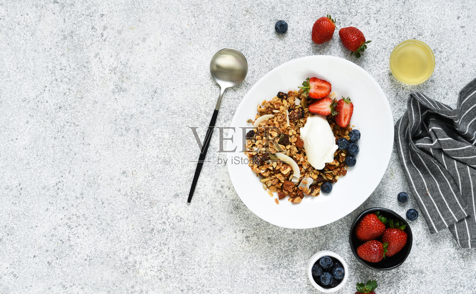 在混凝土背景下的一个盘子里有坚果、蜂蜜和草莓作为早餐。照片摄影图片