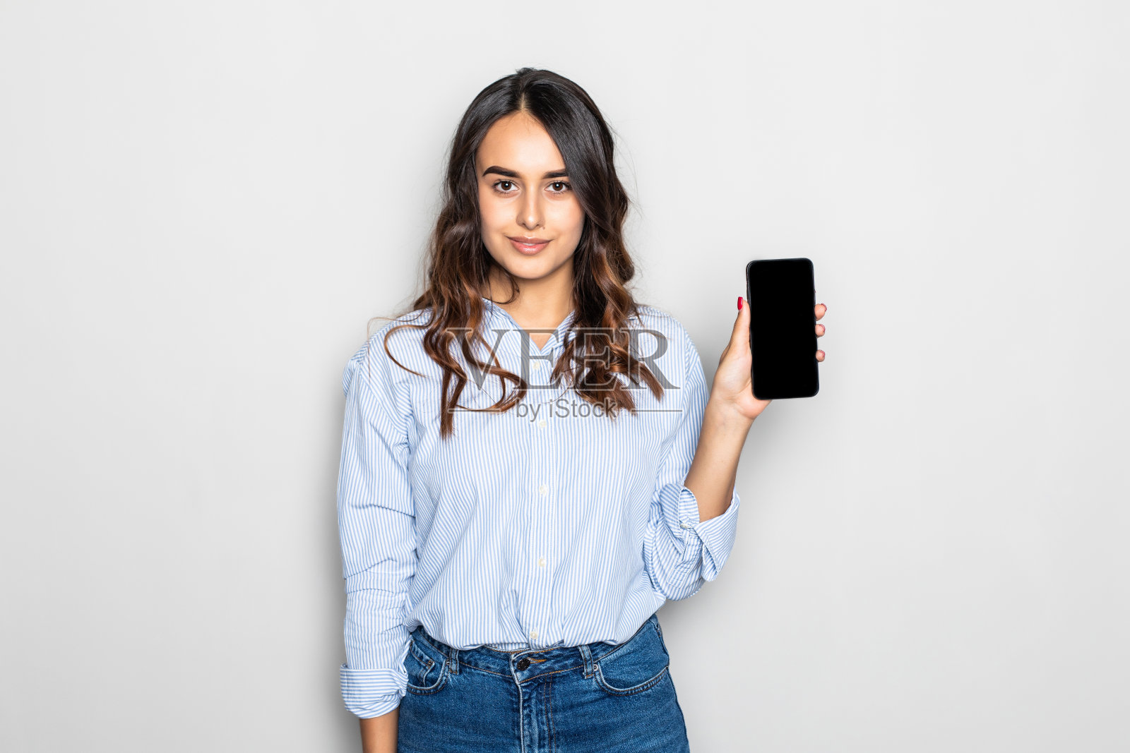 微笑的年轻女孩显示空白的智能手机屏幕孤立在灰色背景照片摄影图片