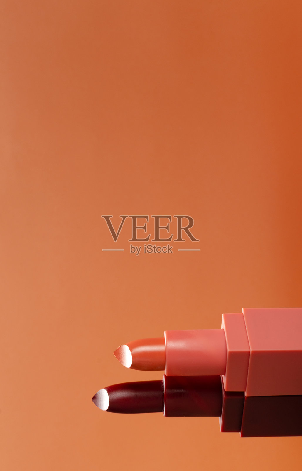 垂直的图像。两支开管的粉红色和深红色的口红映衬着橙色的背景。空的空间照片摄影图片