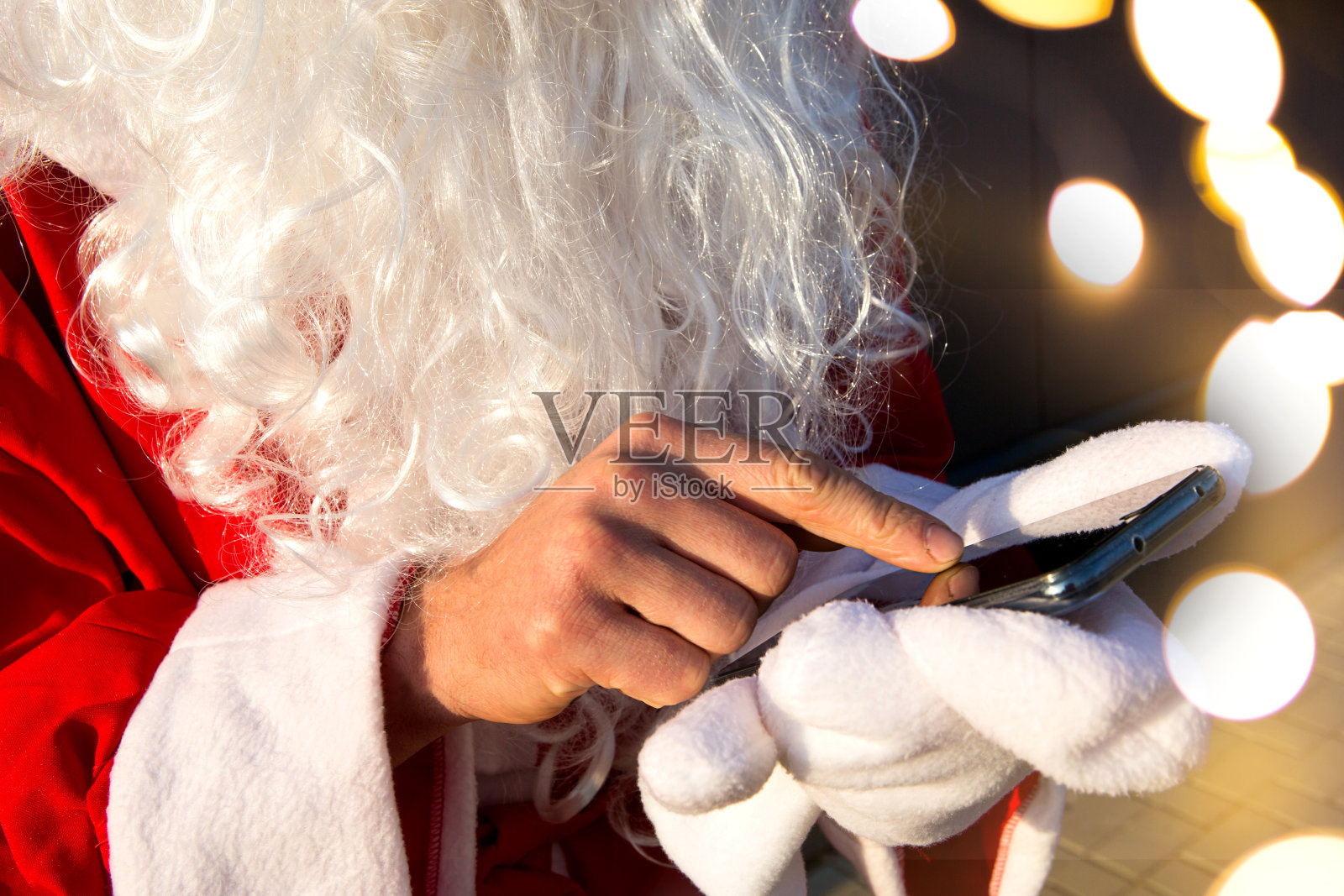 圣诞老人没有戴手套,他的手指在智能手机屏幕上移动。长长的白胡子,红色的西装。现代俄罗斯祖父弗罗斯特。新年订单处理照片摄影图片