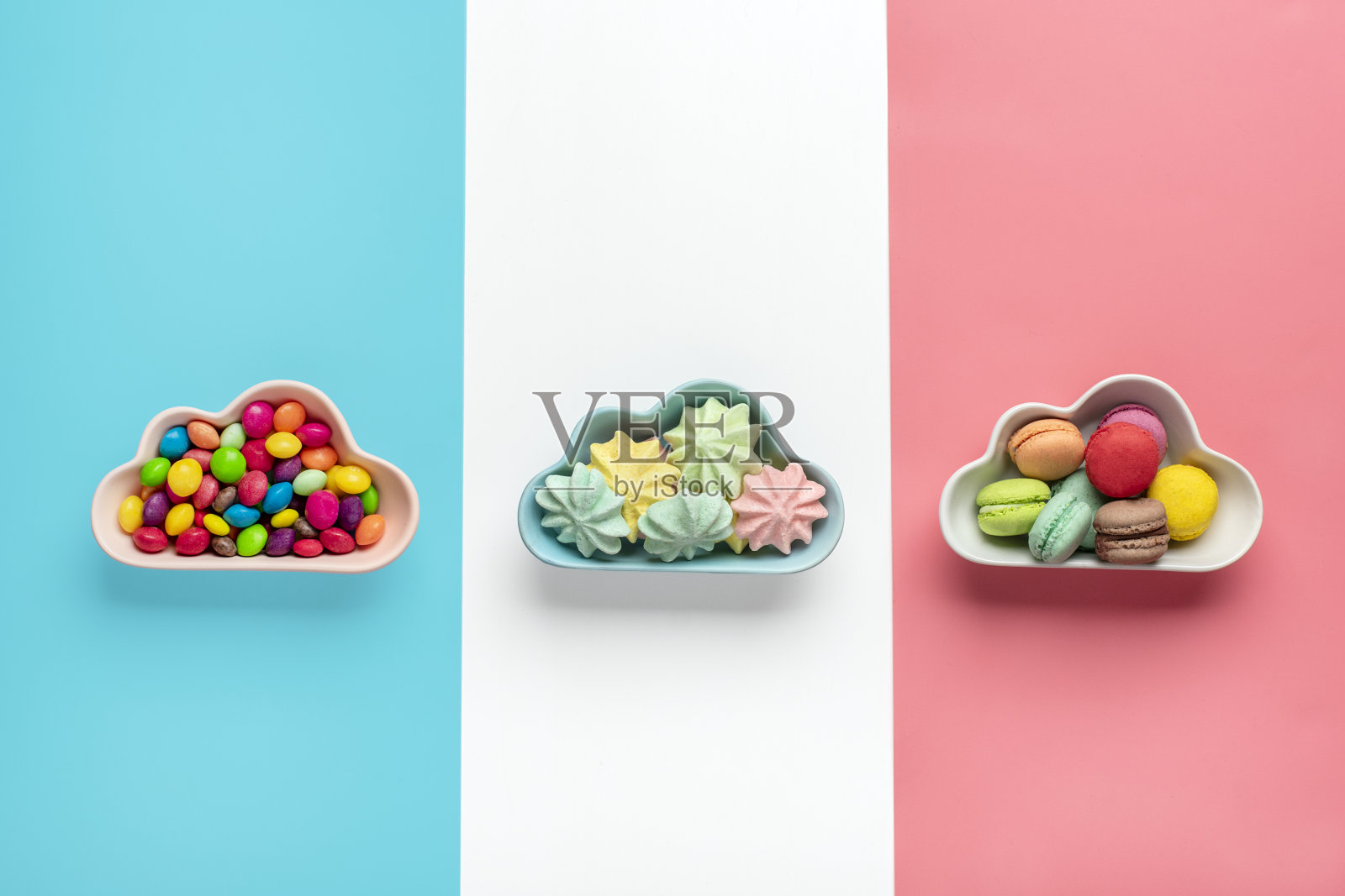 五彩缤纷的糖果-棒棒糖,蛋白酥饼,杏仁饼干在碗状的云孤立在粉红色,白色,蓝色的背景平lay顶视图小山不健康和美味的食物创意概念节日贺卡照片摄影图片