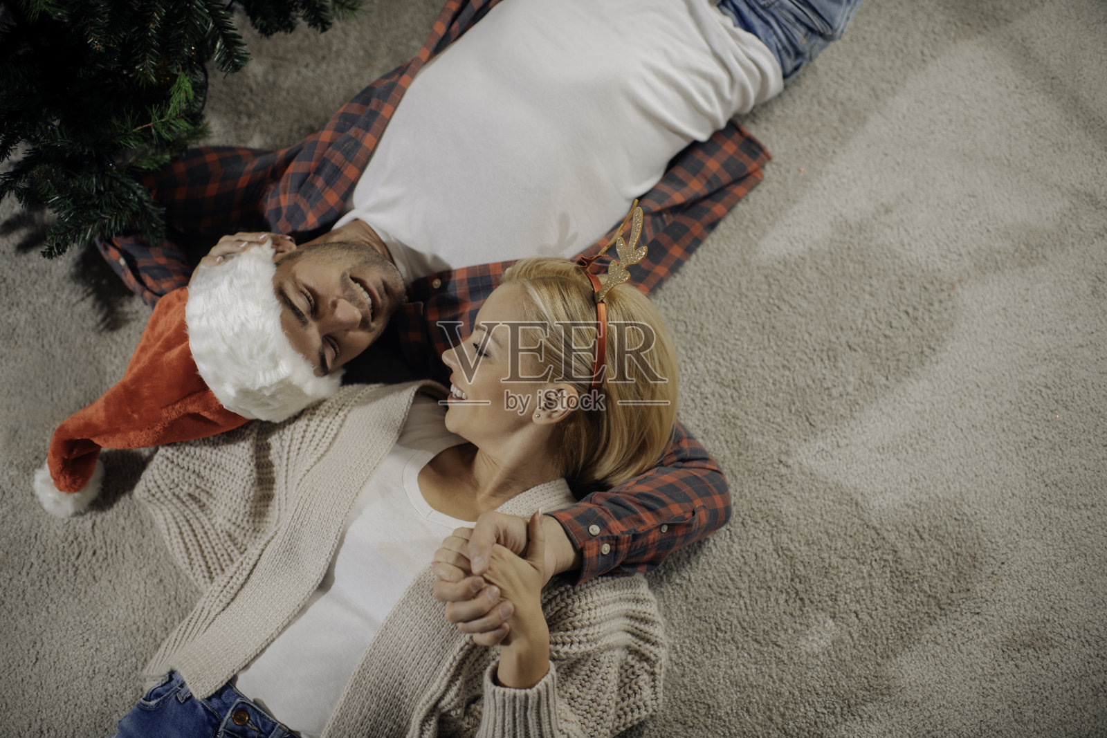 幸福的情侣抱在一起躺在圣诞树旁边的地板上照片摄影图片