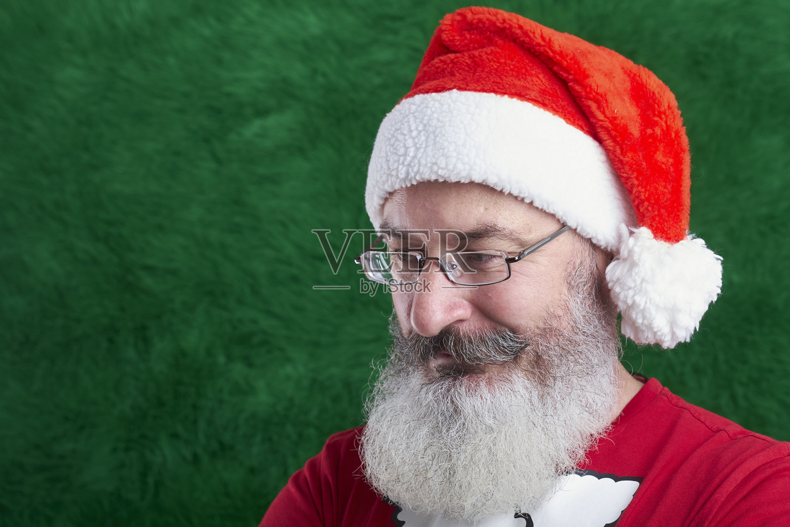成熟的大胡子男子戴着眼镜,脸上戴着圣诞老人帽,人造圣诞树背景,复制空间照片摄影图片